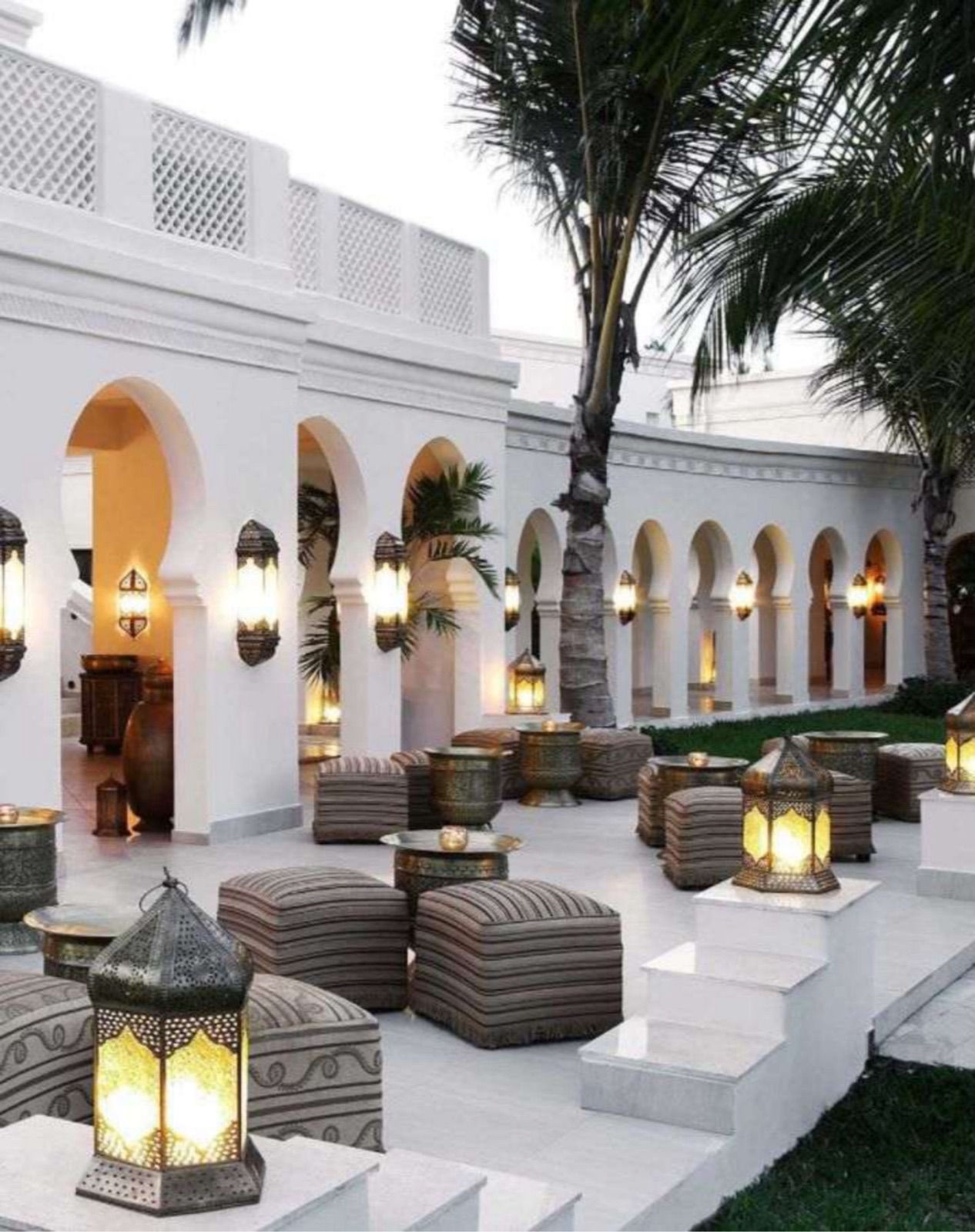 Cour intérieure d'hôtel blanche avec arcades et lanternes au sol
