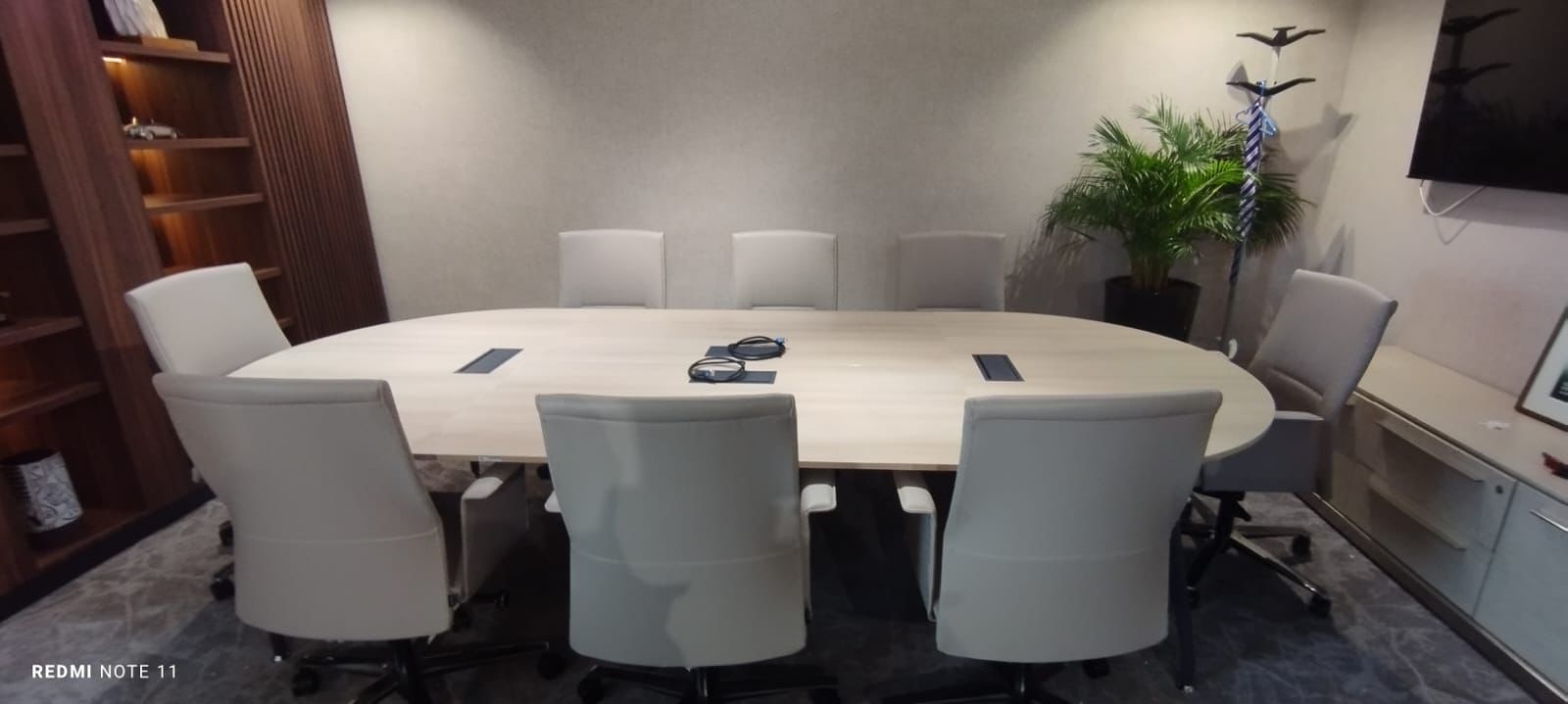 Salle de réunion ovale avec fauteuils gris et bibliothèque noyer